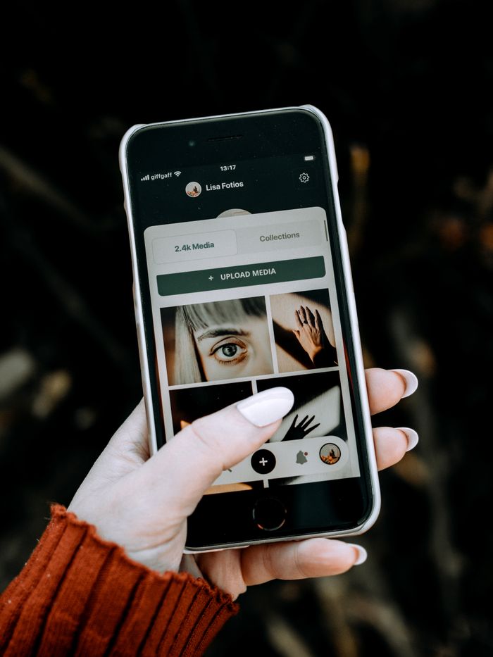 A hand holding a smartphone displaying a photo app with diverse media.